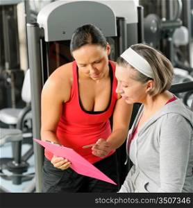Senior woman with personal trainer looking exercise chart at gym