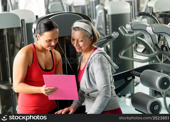 Senior woman with personal trainer looking exercise chart at gym