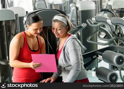 Senior woman with personal trainer looking exercise chart at gym