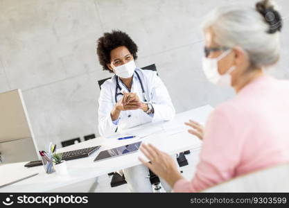 Senior woman with protective facial masks receive news from black female doctor in the office