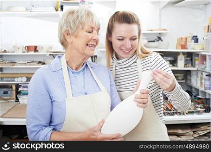 Senior Woman With Teacher Looking At Vase In Pottery Class