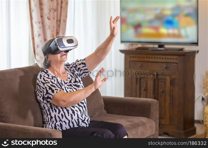 Senior woman with virtual headset or 3d glasses playing videogame at home. Technology, augmented reality, entertainment and people concept. Focus on her hands!