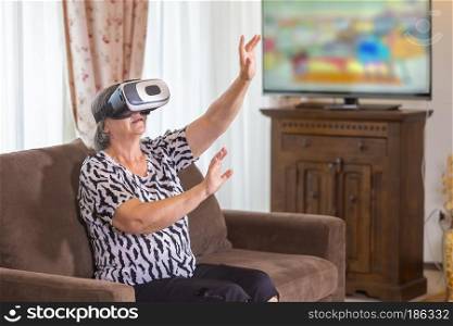 Senior woman with virtual headset or 3d glasses playing videogame at home. Technology, augmented reality, entertainment and people concept. Focus on her hands!