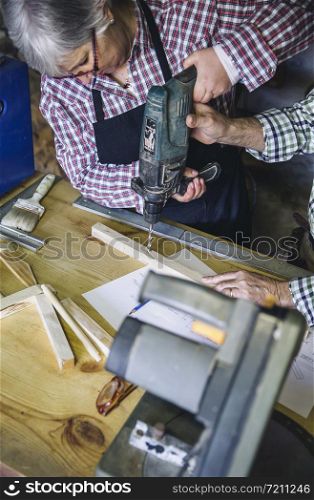 Senior woman working in a carpentry workshop with her husband. Senior couple in a carpentry