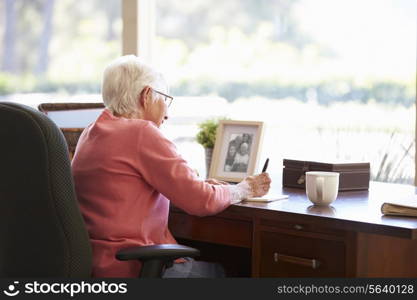 Senior Woman Writing Memoirs In Book At Desk