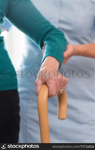 Senior Womans Hands On Walking Stick With Care Worker In Background
