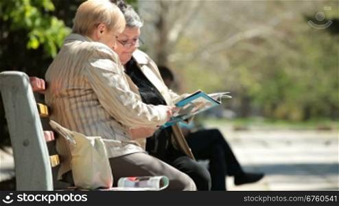 Senior women friends reading glossy magazines in the city park