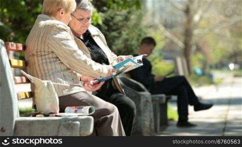 Senior women friends reading magazines in the city park