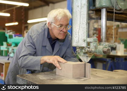 senior worker using machine cutter to saw block of wood
