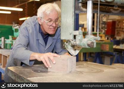 senior worker using machine cutter to saw block of wood