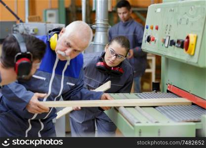 senior worker with apprentices cutting wooden board