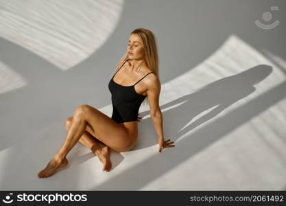Sensitive woman in swimsuit sitting under sunlight on white studio background. Beauty concept. Beautiful woman in swimsuit sitting under sunlight