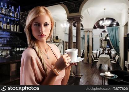 sensual blond girl with hair style drinking a cup of tea in elegant pink dress over dark fashion background