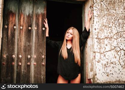Sensual blonde girl in black shirt waiting near a wooden door