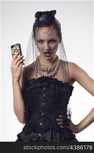 sensual blonde girl with halloween style and make-up wearing gothic dress and dark veil on the face and taking smartphone in the hand