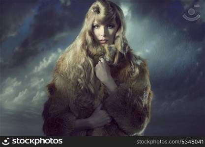 sensual blonde girl with long blonde hair and creative hair-style wearing warm fur coat isolated on background and looking in camera