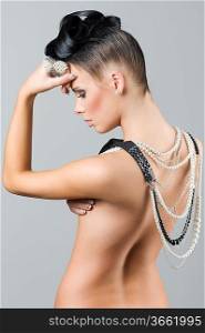 sensual brunette with creative hair style covering her naked back with jewellery in act to think