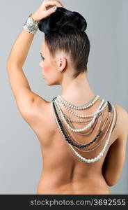 sensual brunette with creative hair style covering her naked shoulder with lots of necklace