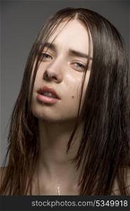 sensual caucasian girl with long wet brown hair and some water drops on the skin of the face. close-up studio portrait