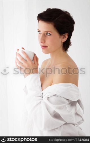 sensual coffee. sensual woman at a window holding coffee wearing a white button down shirt