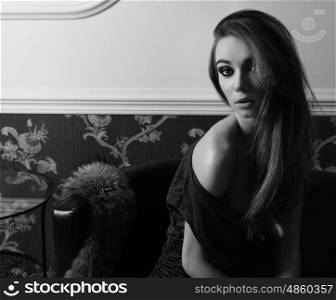 sensual elegant woman with blue dress is sitting on leather sofa near fur. sensual fashion woman with make-up, she is looking in camera with lovely expression . in BW shot
