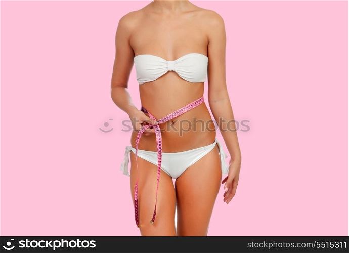 Sensual female body with white bikini anda tape measure on a pink background
