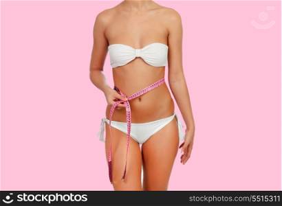Sensual female body with white bikini anda tape measure on a pink background