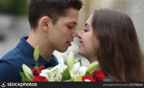 Sensual kiss. Side view of attractive young couple in love holding bouquet of flowers, standing face to face and sharing romantic kiss. Loving couple embracing and kissing outdoors during romantic date.