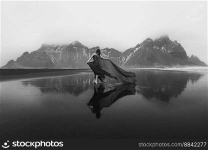 Sensual lady in waving gown on beach monochrome scenic photography. Picture of person with mountains on background. High quality wallpaper. Photo concept for ads, travel blog, magazine, article. Sensual lady in waving gown on beach monochrome scenic photography