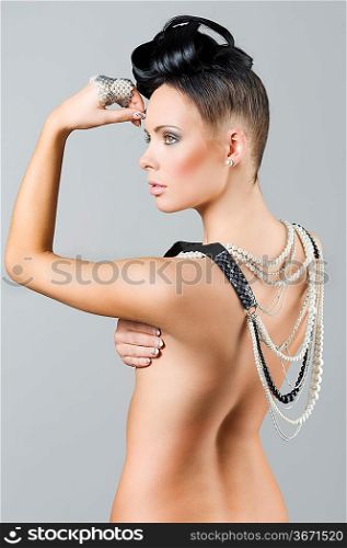 sensual naked brunette with creative hair style covering her back with lots of necklace