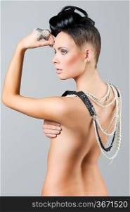 sensual naked brunette with creative hair style covering her back with lots of necklace