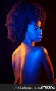 Sensual nude African American female with curly hair looking away over shoulder while standing under colorful neon illumination against black background. Naked black woman under neon light