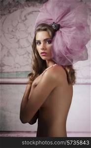 sensual nude brunette girl posing with stylish big tulle accessory on the head, long hair, covering her breast and looking in camera