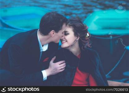 Sensual portrait of happy kissing couple against the blurred background of a lake with boats. Vintage blue toned filter, selective focus.. Blue Toned Portrait Of Happy Couple