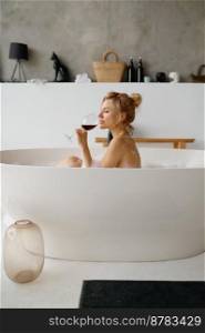 Sensual relaxed woman drinking red wine while taking bath with foam rear view Home spa and rest on weekend or calm evening for stress relief. Sensual relaxed woman drinking red wine while taking bath with foam