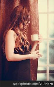 Sensual woman drinking hot coffee beverage at home. Sensual seductive woman in lingerie drinking cup of coffee by curtain and french door window at home. Young girl with hot energizing beverage stay awake. Caffeine energy.