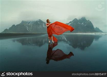 Sensual woman in red clothes on Reynisfjara beach scenic photography. Picture of person with hills on background. High quality wallpaper. Photo concept for ads, travel blog, magazine, article. Sensual woman in red clothes on Reynisfjara beach scenic photography