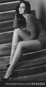 sensual woman with long black hair, sexy red dress and cute legs is sitting on elegant stairs and looking in camera. black and white images .