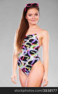 Sensual woman with perfect body wearing fashionable colorful swimwear posing, looking at camera. Long hair, studio shot on gray