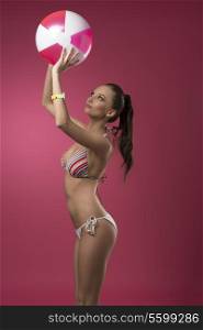 sensual young brunette female with ponytail and bikini playing with beach ball, wearing fashion wrist watch