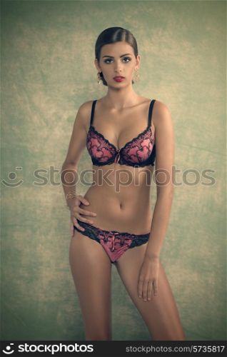 sensual young girl with elegant brown hair-style posing in glamour shoot with pink lace lingerie, perfect body and golden jewellery