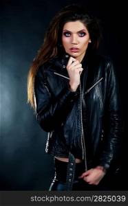 Sensual young woman brunette in black leather jacket standing in studio