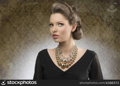 sensual young woman with brown creative hairdo posing in fashion shoot with black dress and bright big necklace