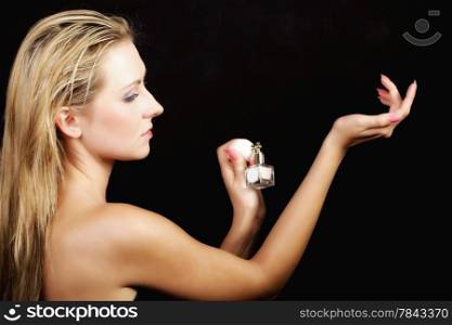 Sensuality concept. Portrait beautiful woman with perfume bottle applying perfume on her wrist, on black background