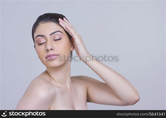 Sensuous young woman touching head over gray background