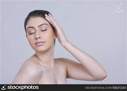 Sensuous young woman touching head over gray background