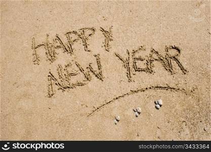 sentence happy new year written in the sand of a beach
