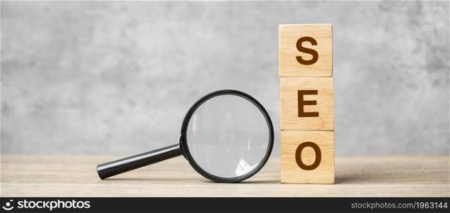 SEO (Search Engine Optimization) text wooden cube blocks and hand holding magnifying glass on table. Idea, Strategy, advertising, marketing, Keyword and Content concept