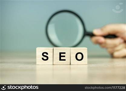 SEO (Search Engine Optimization) text wooden cubes and magnifying glass on wood table background. Idea, Vision, Strategy, Analysis, Keyword and Content concept