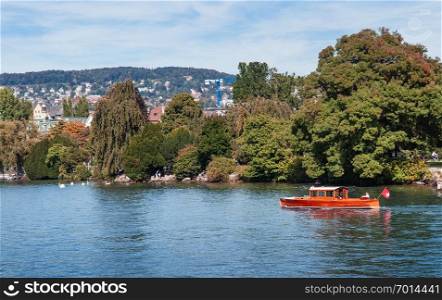 SEP 22, 2013 Zurich, Switzerland - Green lakeside park and classic wooden boat view from lake Zurich on clear sky day in early autumn